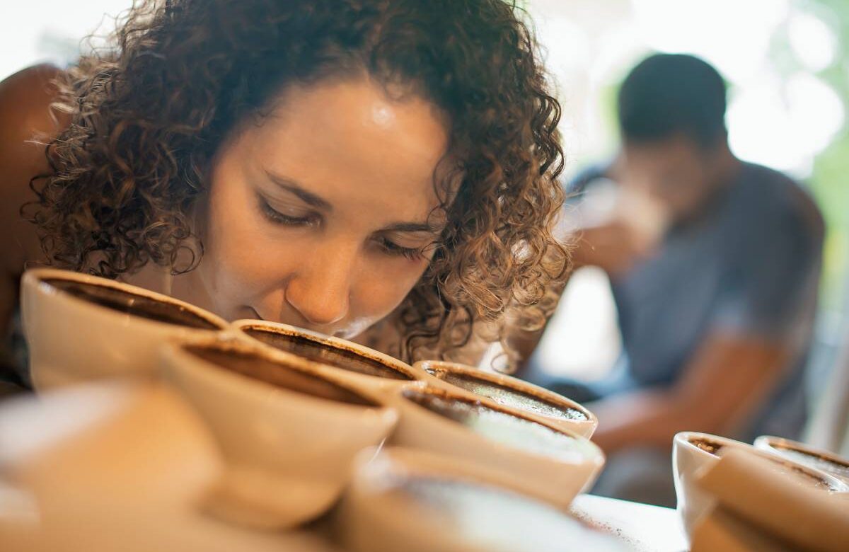 A woman sampling in a coffee processing shed, where staff make coffee in small pots and sample the taste to test the blend.